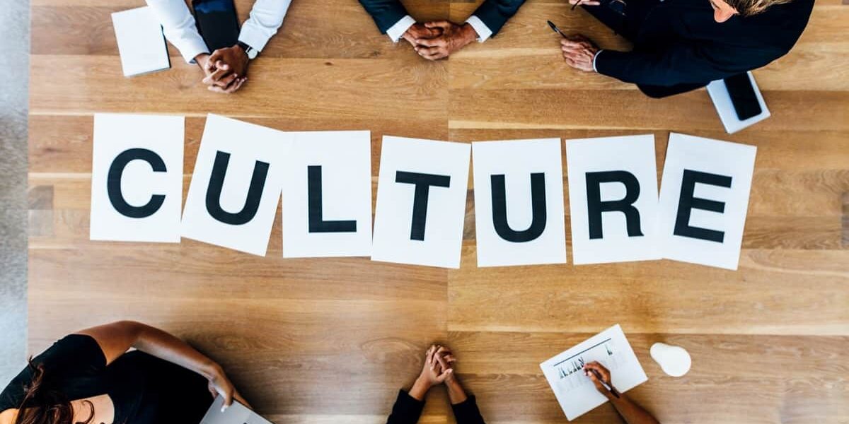 Business people discussing over work culture in meeting Group of business people with alphabets signs forming the word Culture on table. Top view of business people discussing over work culture in a meeting.